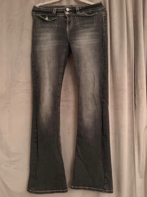 Grå bootcut jeans med kontrastsömmar - Säljer ett par grå bootcut jeans med snyggt slitna detaljer och kontrastsömmar. Jeansen har två framfickor och två bakfickor med dekorativa sömmar 