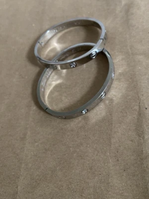 Silverfärgade armband med stenar - Två stilrena armband i silverfärg med infattade gnistrande stenar runt om. Armbanden har en slät, rundad form och en modern look som passar till många olika stilar. Materialet ser ut att vara metall med blanka detaljer. Säljer båda två förr ett pris.
