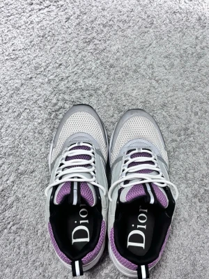 vita och lila sneakers - Snygga sneakers från Zara i vitt, silver och lila med svart detalj och tydlig Zara-logga på plösen. Ovandelen är i mesh och läder för en sportig look. Skorna har vita snören och en robust sula med CD-detalj undertill.