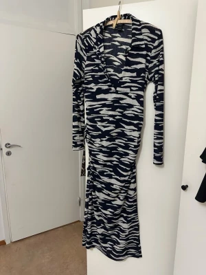 Långärmad mönstrad klänning Lindex - Snygg långklänning från Lindex med zebramönster i mörkblått och vitt. Klänningen har lång ärm, v-ringning och är tillverkad i ett mjukt material som känns skönt mot huden. Perfekt för dig som gillar att sticka ut med coola mönster.