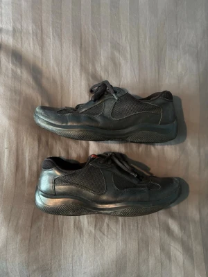 Prada american cups svarta - Säljer ett par svarta prada cups, de är fortfarande i bra skick men de har ”signs of wear” som de jag visar på de 2 sista bilderna. Storleken är 41,5 men eftersom att prada cups är kända för att vara stora i storleken så passar dessa som 43 eller kanske till och med 44.