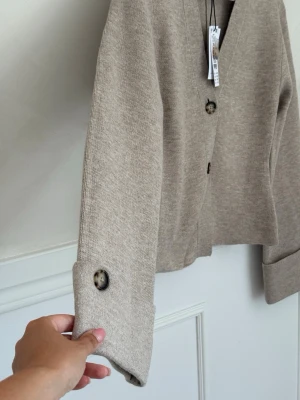 Gina Tricot knitted sculptured cardigan  - Stilren beige kofta från Gina Tricot med v-ringning och stora, marmorerade knappar framtill och vid ärmslut, helt ny med prislapp🤎