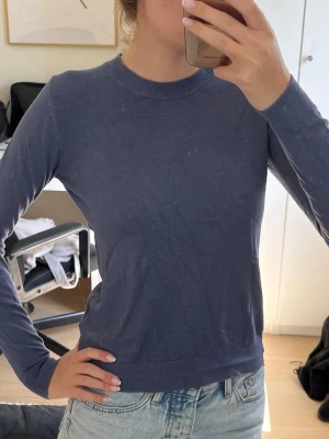 Blå tunnstickad tröja  - Säljer en enkel och stilren blå stickad tröja från 157. Tröjan har rund halsringning, långa ärmar och ribbade muddar vid ärmslut och nederkant. Tunn stickad och mjuk. (Obs min spegel är smutsig)