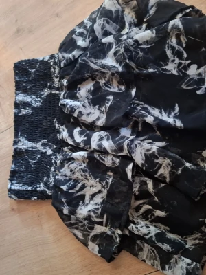 Svart kortkjol med vitt mönster KappAhl - Kortkjol från KappAhl i svart med vitt abstrakt mönster. Kjolen har bred smock i midjan för skön passform och är gjord i ett lätt, luftigt material som ger en snygg volang-effekt.