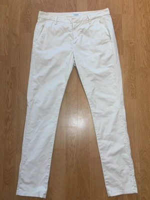 Beiga chinos från Dondup - Snygga beiga chinos från Dondup med raka ben och klassisk passform. Byxorna har fickor fram och bak samt hällor för bälte. Tillverkade i ett mjukt och lätt material som passar perfekt till en avslappnad men stilren look.