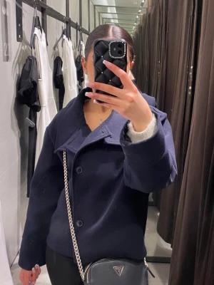 Marinblå kappa - Snygg mörkblå kappa i ull med stora knappar framtill och bred krage. Jackan har lång ärm och en klassisk, stilren look som passar till många outfits. Perfekt för kyligare dagar och höstväder!