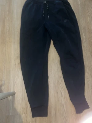 Nike tech  - Svarta mjukisbyxor med smal passform och resår i midjan samt dragsko. Byxorna har ribbade muddar vid bensluten och sidofickor. Perfekta för chill eller träning, tillverkade i mjukt material för maximal komfort.