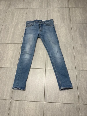 Blå slim fit jeans med slitningar strl 29/32 - Snygga blå slim fit jeans med lätt slitna detaljer och klassisk femficksdesign. Jeansen har en något tvättad look och raka ben. 