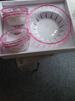 Helt nya. 7 st - Glasskålset med rosa kant - Helt nya. Säljer ett set med glasskålar i transparent glas med dekorativ rosa kant. Setet innehåller en större serveringsskål och flera mindre skålar, perfekta för dessert eller snacks. Skålarna har ett mönster längs kanten och är både snygga och praktiska till köket.