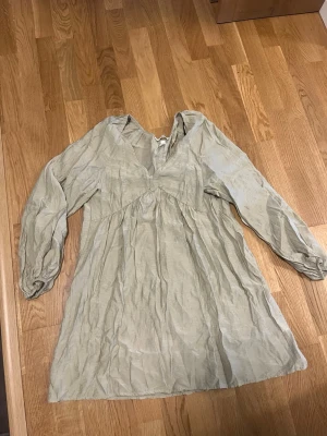 Grön långärmad kortklänning - Luftig grön kortklänning med v-ringning och långa ärmar. Klänningen har en avslappnad passform och är tillverkad i ett lätt material som ger ett mjukt fall. Perfekt för varmare dagar 