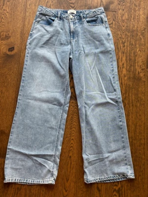 Ljusblå raka jeans från Vanilla Star - Säljer ett par ljusblå jeans från Vanilla Star med rak passform och klassisk femficksdesign. Jeansen har hög midja, bälteshällor och stängs med knapp och dragkedja. Perfekta för en avslappnad och trendig look. De är aldrig använda och köptes i USA