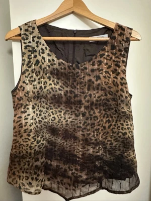 Leopardmönstrad linnetopp Merrytime - Ärmlös linnetopp från Merrytime med leopardmönster i bruna och svarta nyanser. Toppen har rund halsringning och är tillverkad i ett lätt, transparent syntetmaterial som ger en luftig känsla.