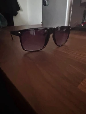 Tonade glasögon - Snygga svarta solglasögon med breda bågar och fyrkantig form. Glasen är mörka och tonade, vilket ger en cool look. Perfekta för att höja stilen på sommaren eller när solen skiner. Klassisk design som passar till det mesta.