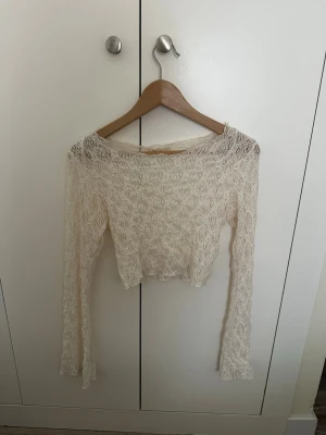 Vit spetsig croppad långärmad topp - Säljer en vit croppad topp i spets med lång ärm och rund hals. Toppen har ett romantiskt och trendigt utseende med transparent spetsmaterial och passar perfekt till jeans eller kjol. Perfekt för dig som vill ha en feminin och stilren look.