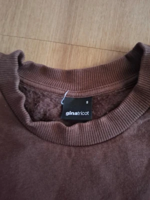 Brun sweatshirt från Gina Tricot - Mysig brun sweatshirt från Gina Tricot i storlek S. Tröjan har rund halsringning, ribbade muddar vid ärmslut och nederkant samt en enkel, stilren design. Perfekt för en avslappnad och trendig look.