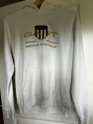 Vit hoodie från Gant med tryck - Säljer en vit hoodie från Gant med broderat Gant-emblem på bröstet. Hoodien har huva och känguruficka. Perfekt för en sportig och avslappnad stil. Tröjan är storlek 170 cm som passar som en S. 