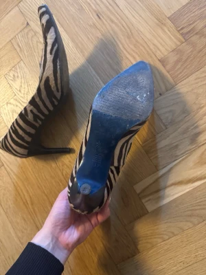 Zebramönstrade pumps med spetsig tå - Snygga pumps med zebramönster i svart och beige. Skorna har spetsig tå och smal klack för en trendig look. Materialet ser ut att vara textil med djurmönster. Vintage, köpes i befintligt skick!