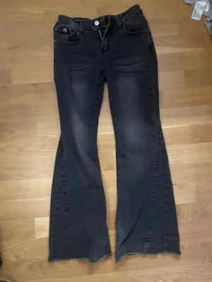 Svarta bootcut jeans med rå kant - Säljer ett par svarta bootcut jeans med rå, fransig kant nertill. Jeansen har en klassisk femficksmodell och är tillverkade i denim med lätt tvättade partier. Perfekta för dig som gillar en avslappnad och trendig stil. Passar någon runt 160 cm