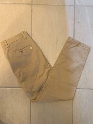 Hansen & Jacob chinos beige herr - Snygga beige chinos i storlek W33 L32 med klassisk passform och en bakficka med knapp och liten metallogo. Från märket Hansen & Jacob med ett nypris på 2000kr. Skriv gärna vid fler funderingar:)