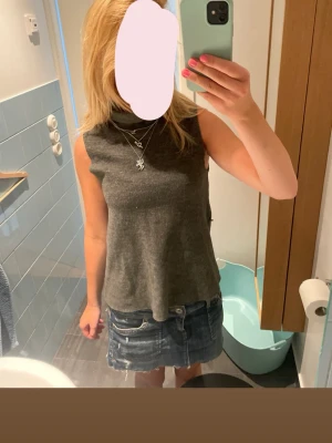 Mörkgrå ärmlös polotopp - Snygg mörkgrå polotopp i mjukt material. Toppen är ärmlös och har en hög krage som ger en clean look. Passar perfekt till jeans eller kjol för en chill och stilren outfit.