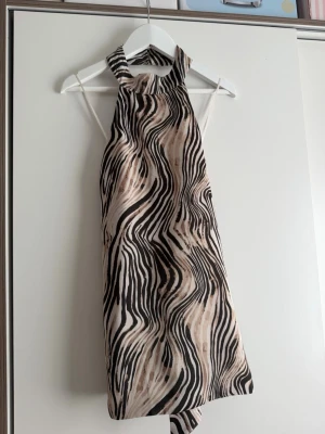 Zebramönstrad halterneck topp - Säljer en snygg zebramönstrad halterneck topp i beige och svart från bikbok!! Toppen har öppen rygg och knyt i ryggen! använd en gång💗
