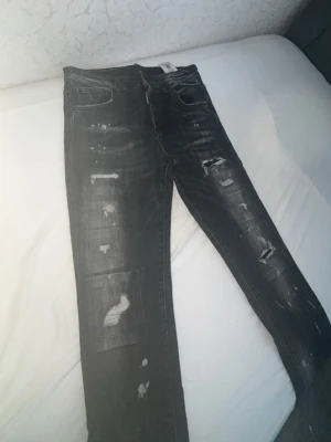 Dsquared2 jeans - Säljer ett par svarta jeans från Dsquared2 med slitningar och distressed detaljer. Jeansen har smal passform, klassisk femficksdesign och bälteshällor. Perfekta för dig som gillar en edgy och trendig stil.
