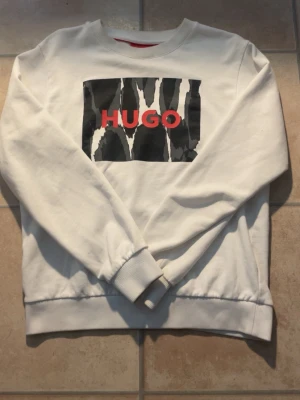 Vit sweatshirt från HUGO, XS - En jättefin tröja som går att matcha dina outfits med hur bra som helst, skicket e skit bra men det finns ett litet hål vid axeln me enkel syning så e den som vanligt, ordinarie pris ligger på 1200