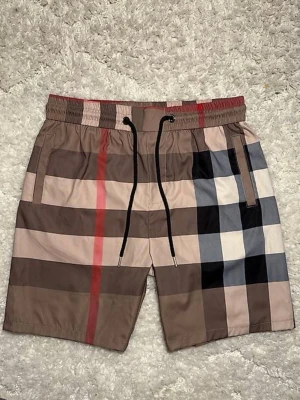 Rutiga shorts med dragsko - Snygga shorts med klassiskt rutigt mönster i beige, brunt, svart, vitt och rött. De har elastisk midja med svart dragsko och sidofickor. Perfekta för en avslappnad och trendig stil.