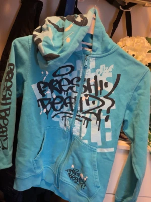 Turkos hoodie med graffiti-tryck - Säljer en turkos hoodie med dragkedja och stor huva. Hoodien har coola graffiti-inspirerade tryck i svart och vitt på bröstet, ärmen och huvan. Fickor framtill och ribbade muddar. Perfekt för dig som gillar streetwear och vill sticka ut. H&m hoodie, men ganska så liten. Bra för dig om du är lite kortare än vanligt. Både för män o kvinnor