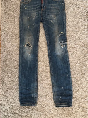 Blå slitna skinny jeans med hål - Säljer ett par blå skinny jeans med slitningar, hål på ena knät och distressed detaljer över hela byxan. Jeansen har klassisk femficksmodell och är tillverkade i denim med en tvättad look. Perfekta för en avslappnad och trendig stil.
