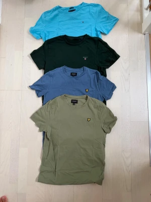 Fyra färgglada märkes t-shirts - Fyra t-shirts i olika färger: ljusblå, mörkgrön, blå och olivgrön. Alla har rund hals och korta ärmar. Några har små broderade loggor på bröstet. Perfekta för en avslappnad och stilren vardagslook. Storlek på lyle & scott 14-15 år, Gant 170 barn och Tommy hilfiger storlek 176. Säjer alla men kan köpas separat ochså
