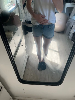 Ljusblå denimshorts - Säljer ett par ljusblå denimshorts med låg midja och klassisk femficksdesign. Shortsen har en avslappnad passform och är perfekta för varma dagar. Stängs med knapp och dragkedja framtill.