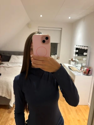 Mörkblå långärmad polo body  - Säljer en mörkblå, långärmad polobody med slim passform. Bodyn har en hög krage och är tillverkad i ett mjukt, stretchigt material som sitter snyggt mot kroppen. Perfekt att styla med jeans eller kjol för en clean look.