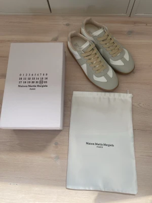 Vita och beige sneakers  - Snygga sneakers i vitt och beige med klassisk design. Skorna har ovandel i läder och mocka, samt beigea snören och en brun gummisula med mönstrad undersida för bra grepp. Perfekta för en clean och stilren look.