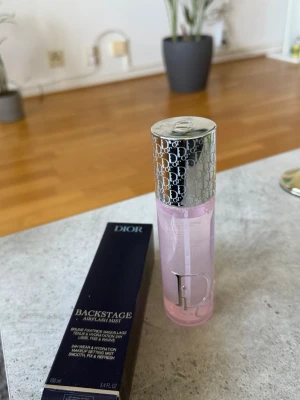 Dior Backstage Airflash Face Mist - Dior Backstage Airflash Mist är en ansiktsspray som fixerar makeup och återfuktar huden i upp till 24 timmar. Kommer i en elegant cylinderformad flaska med silverfärgat lock och rosa vätska. Perfekt för en fräsch och återfuktad look hela dagen.