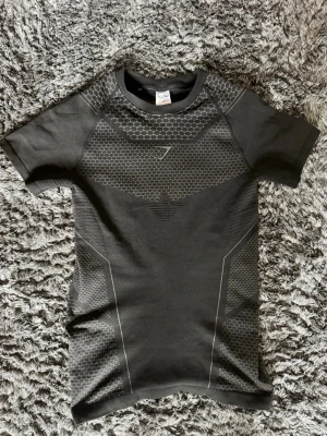 OG Gymshark Onyx V4 ÄKTA och sällsynt - Snygg ÄKTA svart Onyx v4 från Gymshark med korta ärmar och coolt hexagonmönster i grått. Tröjan har en tight passform och är tillverkad i ett stretchigt funktionsmaterial som andas, perfekt för gymmet eller löpning. Väldigt sällsynt och produceras inte längre. Pris kan diskuteras! 