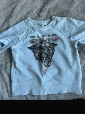 Ljusblå sweatshirt Zadig & Voltaire - Cool ljusblå sweatshirt från Zadig & Voltaire med ett stort tryck av en panter och glittriga detaljer framtill. Tröjan har rund halsringning och långa ärmar. Perfekt för dig som gillar streetstyle och statementplagg.