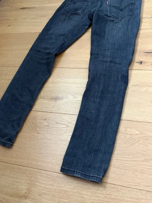 Levis - Säljer ett par mörkblå jeans med rak passform och klassisk femficksdesign. Jeansen har subtila slitningar och kontrastsömmar. Perfekta till vardags för en avslappnad men snygg look.