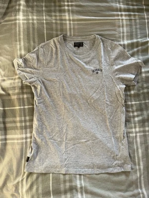 Grå t-shirt från Morris - Snygg grå t-shirt från Morris med diskret logga på bröstet. Klassisk rund halsringning och korta ärmar. Tillverkad i mjuk bomull som känns skön mot huden. Perfekt basplagg till garderoben.