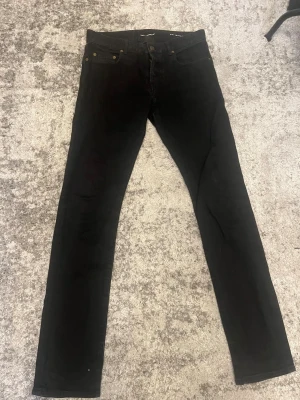 Svarta skinny jeans - Säljer ett par svarta skinny jeans med klassisk femficksdesign och smal passform. Jeansen har knappgylf och nitar i metall vid fickorna. Perfekta för dig som gillar en stilren och enkel look.
