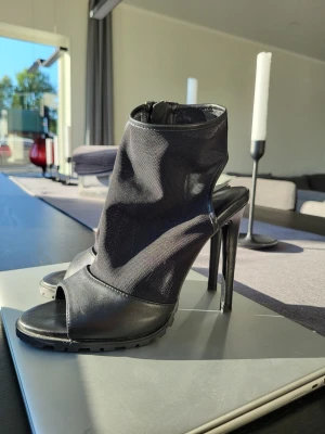 Zara Women pumps med hög klack - Snygga svarta pumps med öppen tå och hög stilettklack. Skorna har en modern design med täckt ovandel i textil och detaljer i läderimitation. Dragkedja baktill för enkel påtagning och grov sula för extra grepp.