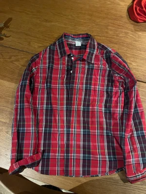 Röd rutig skjorta  - Klassisk röd rutig skjorta med långa ärmar och knappar framtill. Skjortan har en avslappnad passform och är tillverkad i mjukt bomullstyg. Perfekt för en casual look och enkel att matcha med jeans eller chinos.