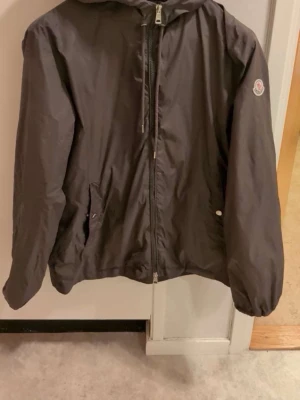 Moncler Vindjacka, grön - Säljer min snygga vindjacka med mörkgrön färg. Perfekt för blåsiga dagar. Riktigt stilig jacka med detaljer på luvan. Exklusiv utav hög kvalitet. Fint skick finns endast två små skavanker se på bilderna’ syns inte vid användning. Storlek 3 sitter som M passa på! 