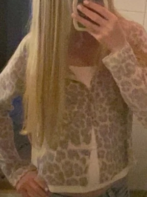 Beige leopardmönstrad kofta - Säljer en beige kofta med leopardmönster och rund hals. Koftan har knäppning framtill med vita knappar och är tillverkad i ett tunt, mjukt material. Fint att ha ett linne under! Storlek M men passar mig som är XS och känns även som XS eller S