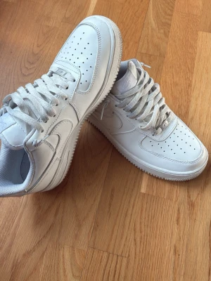 Helvita airforce 1 - Säljer ett par helvita sneakers med klassisk siluett och perforerad tåbox. Skorna har vita snören, diskreta sömmar och är tillverkade i slätt läder. Passar perfekt till streetwear och har en tidlös look. Knappt använda. Säljer billigt pga att jag behöver bli av med dem. Vid frågor hör av er. 