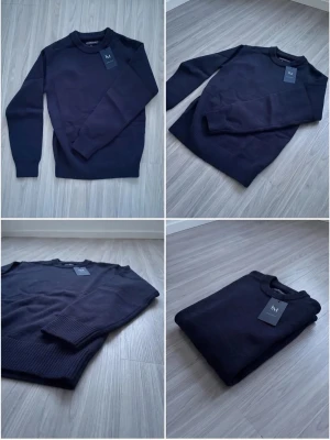 Mörkblå stickad tröja - Snygg mörkblå stickad tröja med rund hals och ribbade muddar vid ärmslut och nederkant. Tröjan har en enkel och stilren design som passar perfekt till många olika outfits. Materialet ser mjukt och bekvämt ut.
