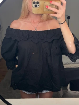 Svart offshoulder blus med spets - Säljer en svart offshoulder blus med bred volangkant och broderade blommor. Blusen har trekvartsärm med spetsdetaljer och är luftig och skön. 