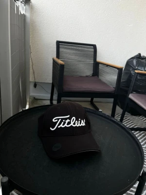 Svart Titleist keps med brodyr - Säljer en svart keps från Titleist med vit broderad logga framtill. Klassisk böjd skärm och justerbar baksida. Tillverkad i ett ventilerande tyg som passar perfekt för golf eller vardagsstil.
