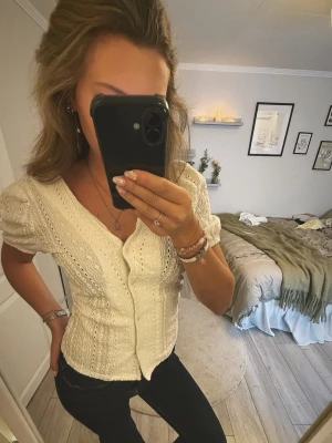 Vit blus med broderade detaljer - Söt vit blus med v-ringning och broderade hålmönster. Blusen har puffiga korta ärmar och knäppning framtill. Tillverkad i ett lätt och luftigt tyg som ger en romantisk känsla. Perfekt att styla med jeans eller kjol för en trendig look.