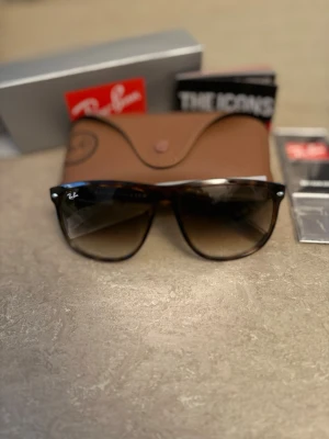 Ray-Ban svarta solglasögon - Snygga svarta solglasögon från Ray-Ban med klassisk rektangulär form och mörka glas. Bågarna är i plast och kommer med originalfodral och tillbehör. Perfekta för att höja din stil i solen.